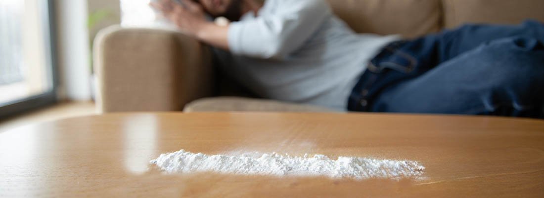 Признак употребления На столе белый порошок, сзади сиди мужчина на диване